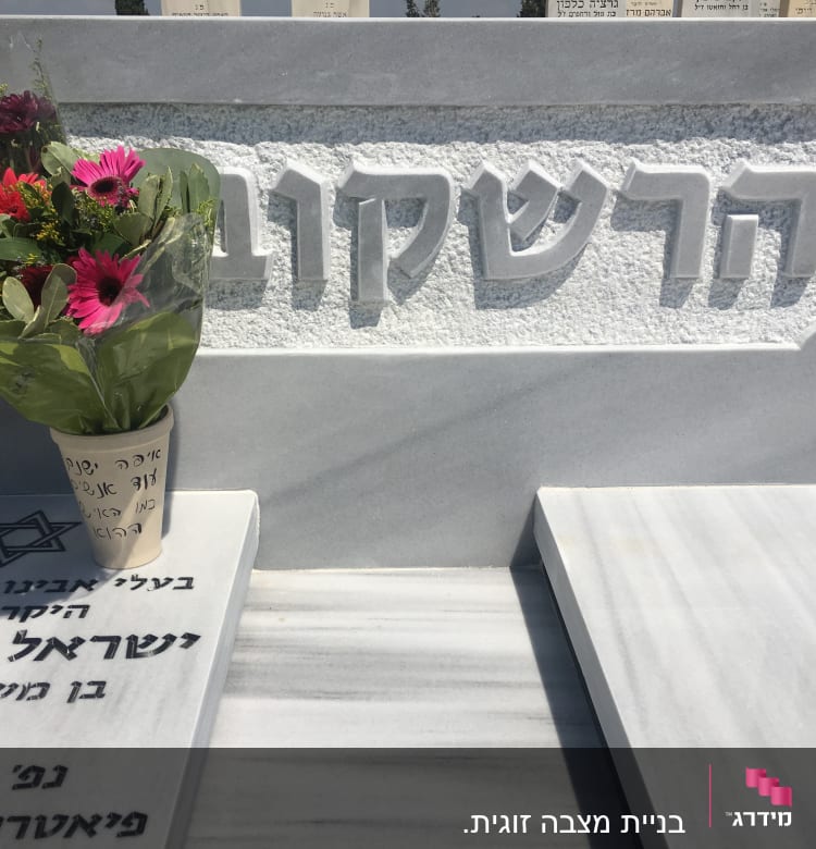 מצבה עם כיתוב בעברית וזר פרחים צבעוני